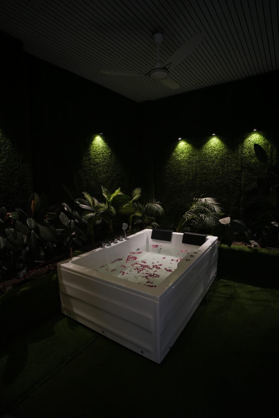Um quarto de spa com uma banheira grande, plantas verdes e um ventilador de teto.