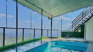 A swimming pool with a view of the sea, surrounded by a covered area with a metal roof and a staircase leading to an upper level. - Hill Top Heaven By Elvora Hotels & Resorts (Kasauli)