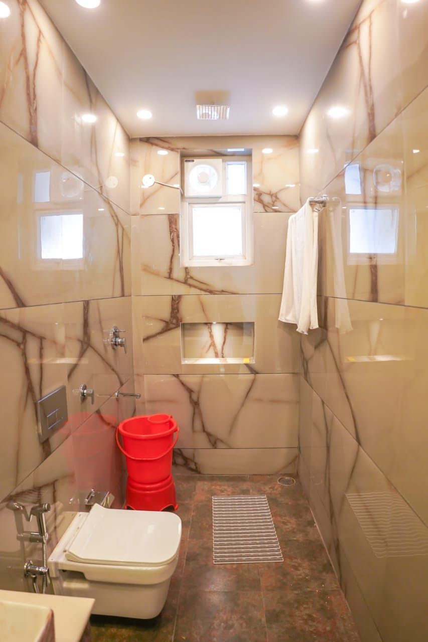 Un baño con paredes de mármol, un inodoro, un bidé y un cubo rojo.