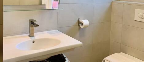 A modern bathroom with a white sink, mirror, and toilet.