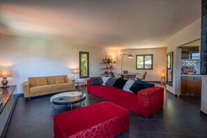 A modern living room with a sofa, a red couch, a round coffee table, and a dining area with chairs and a table. - residence Guddelmoni (Propriano)