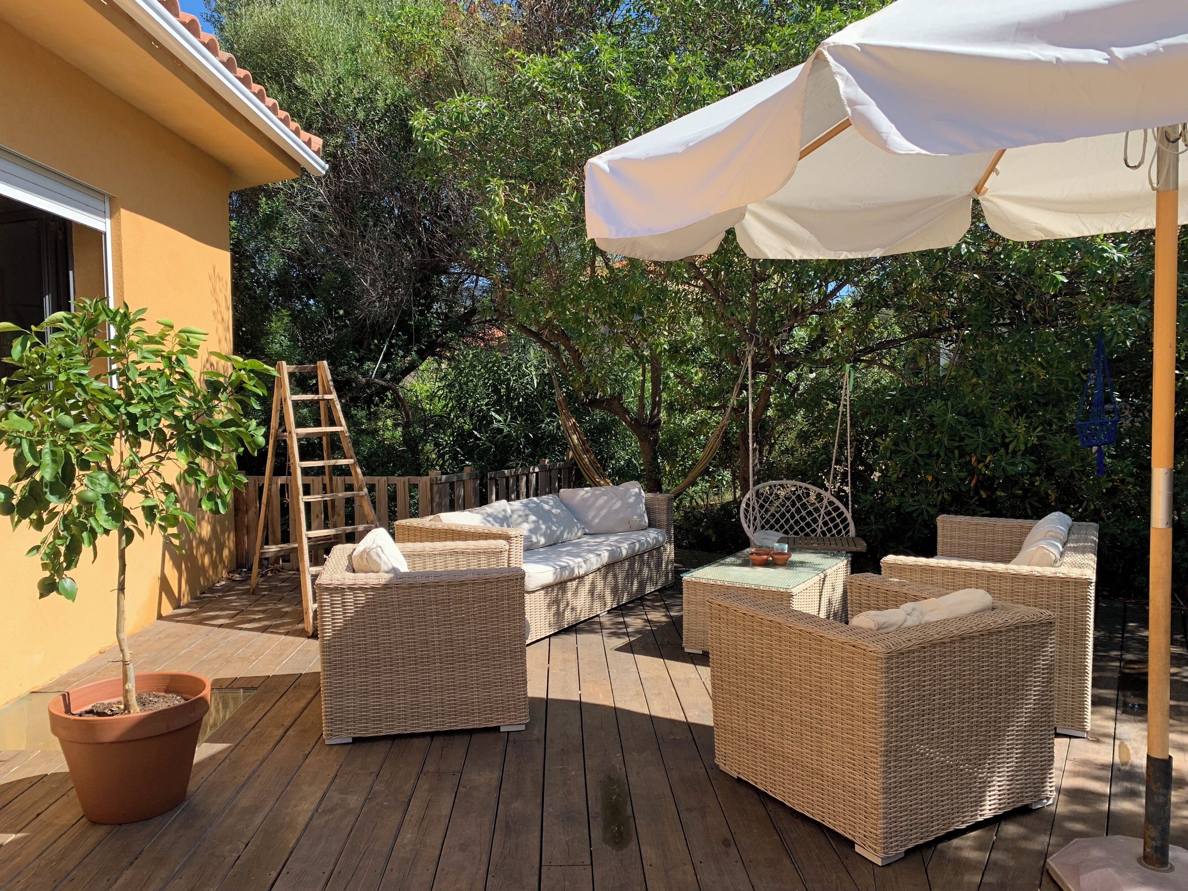 An outdoor patio with wicker furniture, a white umbrella, and a wooden deck.