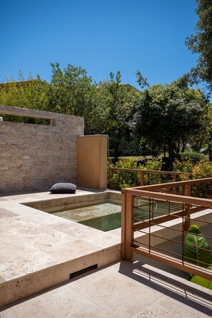 A modern outdoor pool area with a stone wall, a wooden deck, and a metal railing. - residence Guddelmoni (Propriano)
