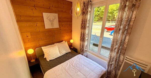 A cozy room with a wooden headboard, a bed with white bedding, two bedside lamps, and a window with patterned curtains.