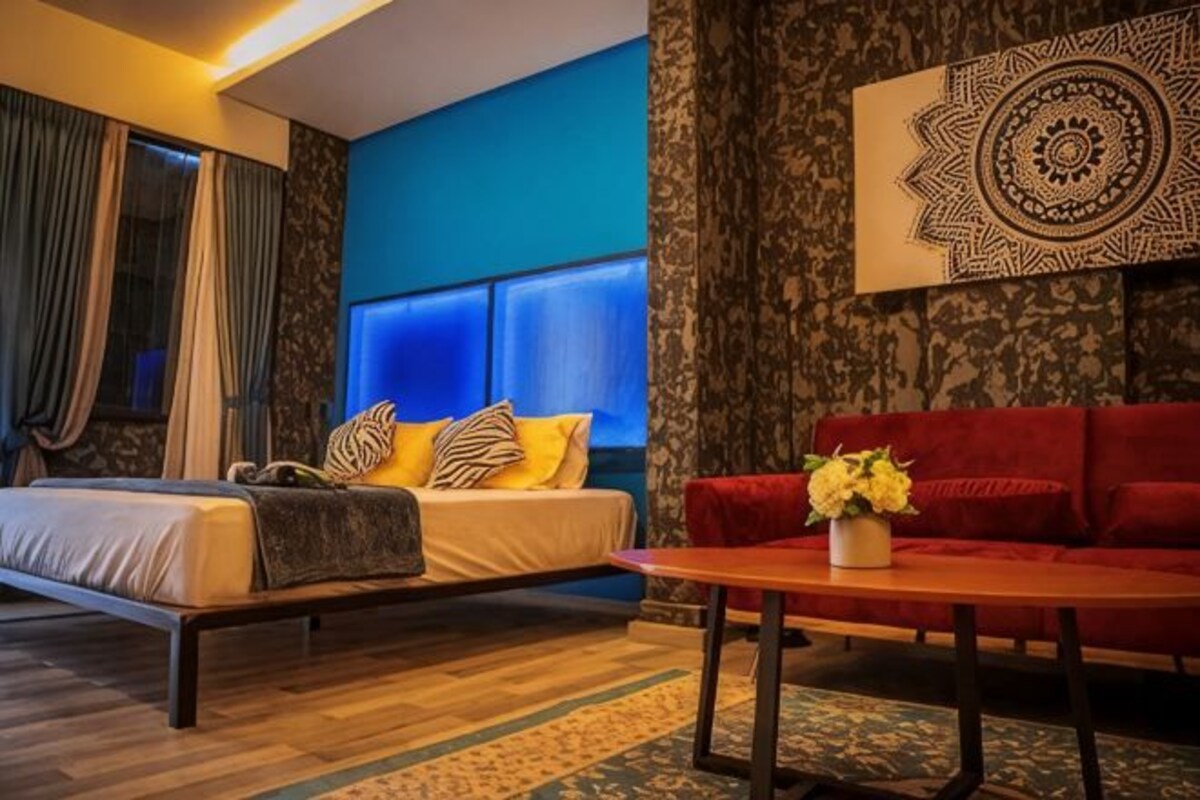 A bedroom with a bed, a red sofa, a coffee table, and a wall with a decorative pattern.
