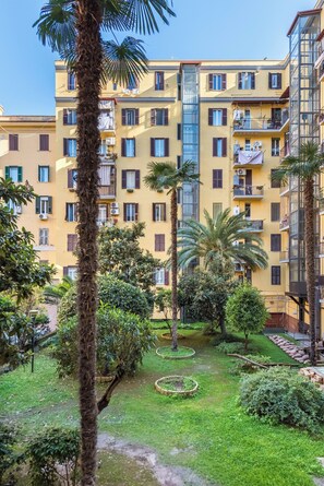 Un edificio amarillo de varios pisos con balcones, rodeado de vegetación exuberante y palmeras.
