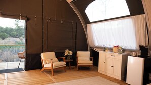 Un interior acogedor con una terraza de madera, dos sillas, una mesita con flores, una kitchenette y un ventanal grande.
