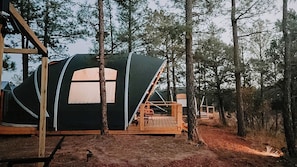 A forested campsite with a large, black tent with a white window and a wooden deck.