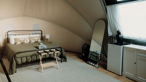 Una tienda de campaña compacta y bien iluminada, con cama, lámparas de noche, un escritorio pequeño y una kitchenette compacta.