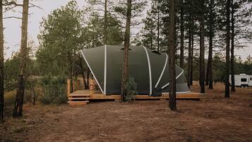A modern, tent-like structure with a wooden deck in a forested area.