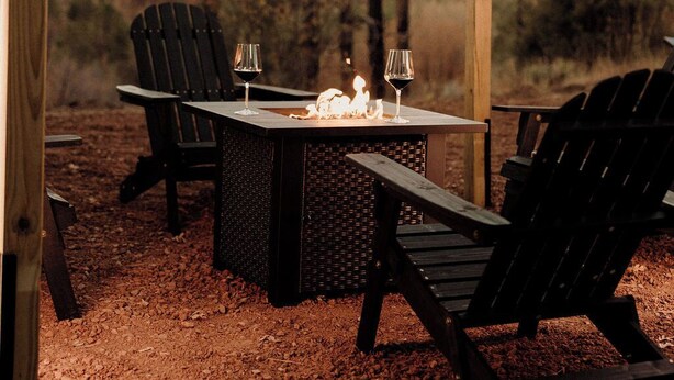Una pérgola de madera al aire libre con luces colgantes, una mesa y dos sillas Adirondack.