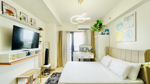 Ein Hotelzimmer mit Bett, Fernseher, Schreibtisch, Spiegel und Pflanze.