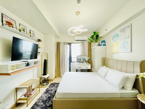 Una habitación de hotel con cama, televisor, escritorio, espejo y planta.