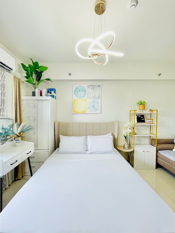 A modern hotel room with a bed, bedside tables, a desk, and a wall-mounted air conditioner.