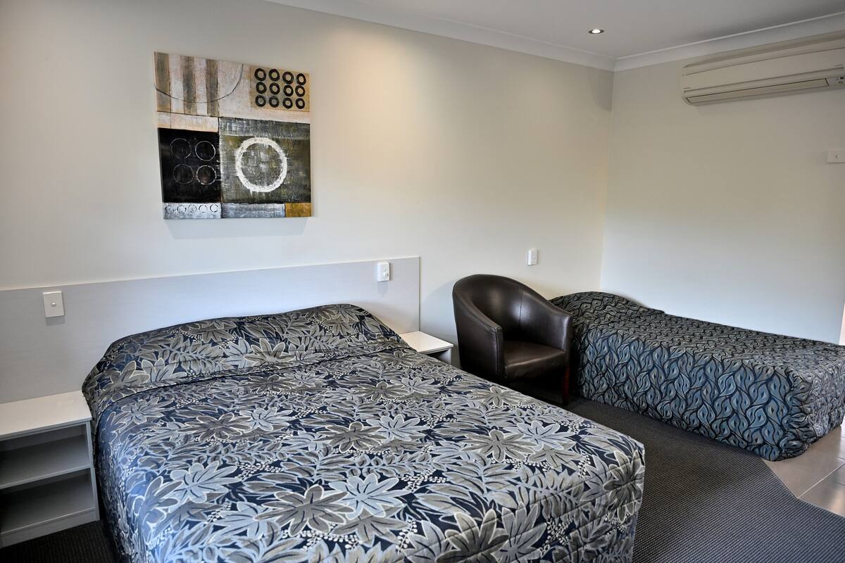 A hotel room with two beds, a small table, a chair, and a wall art piece.