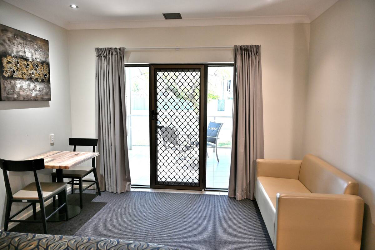 A modern living room with a sofa, a dining table with chairs, and a sliding glass door leading to an outdoor area.