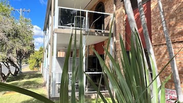 Un edificio de dos plantas con balcón, paredes de ladrillo y cielo despejado.
