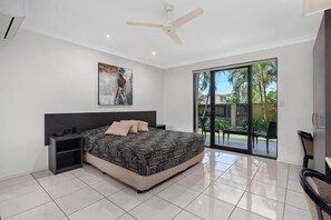 A bedroom with a bed, a nightstand, a ceiling fan, a painting, and a sliding glass door leading to a balcony.