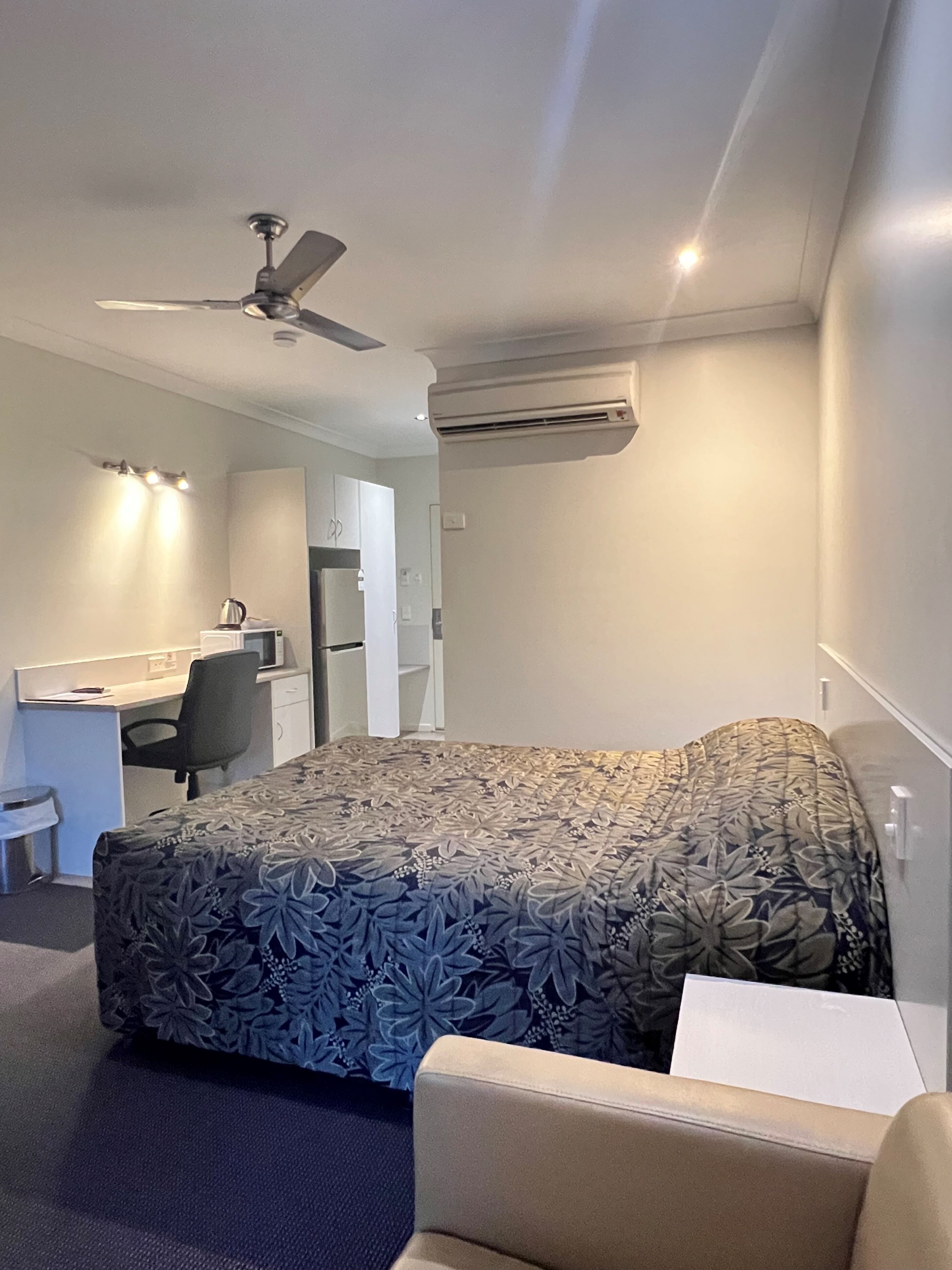 Habitación de hotel con cama, escritorio, silla, aire acondicionado y ventilador de techo.