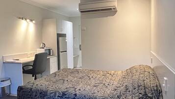 Habitación de hotel con cama, escritorio, silla, aire acondicionado y ventilador de techo.
