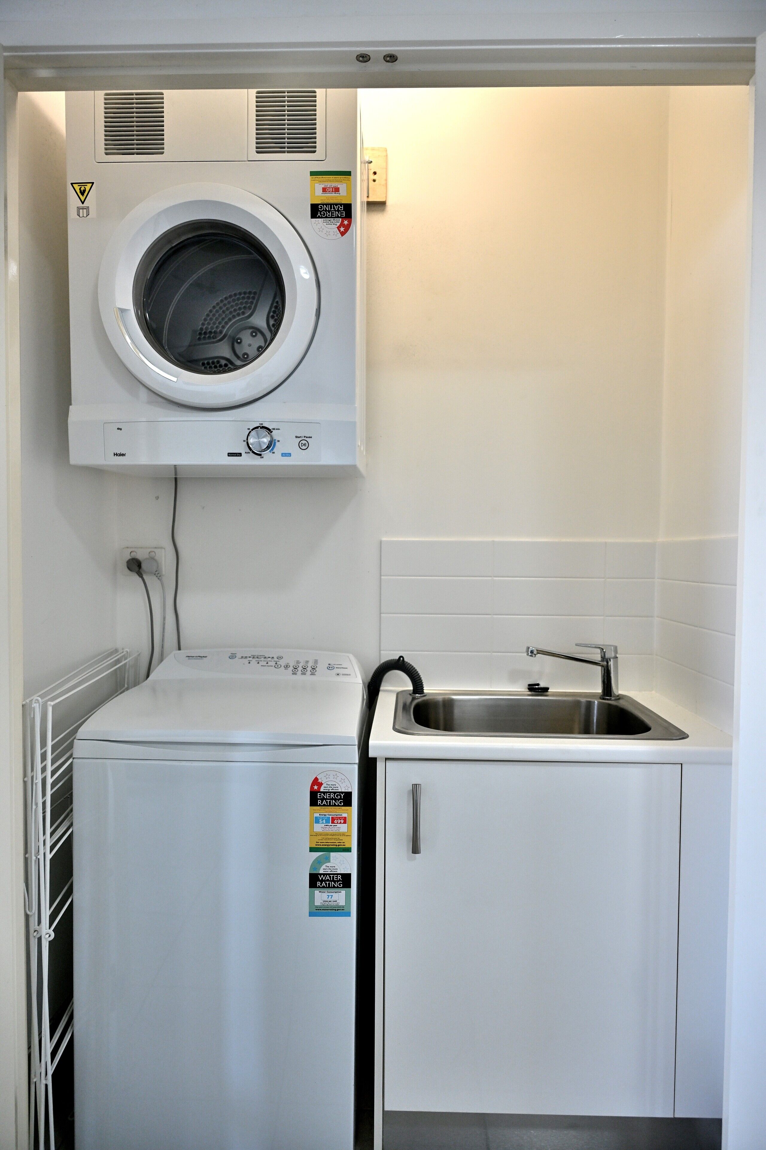A compact laundry room with a front-loading washing machine, a dryer, and a sink.