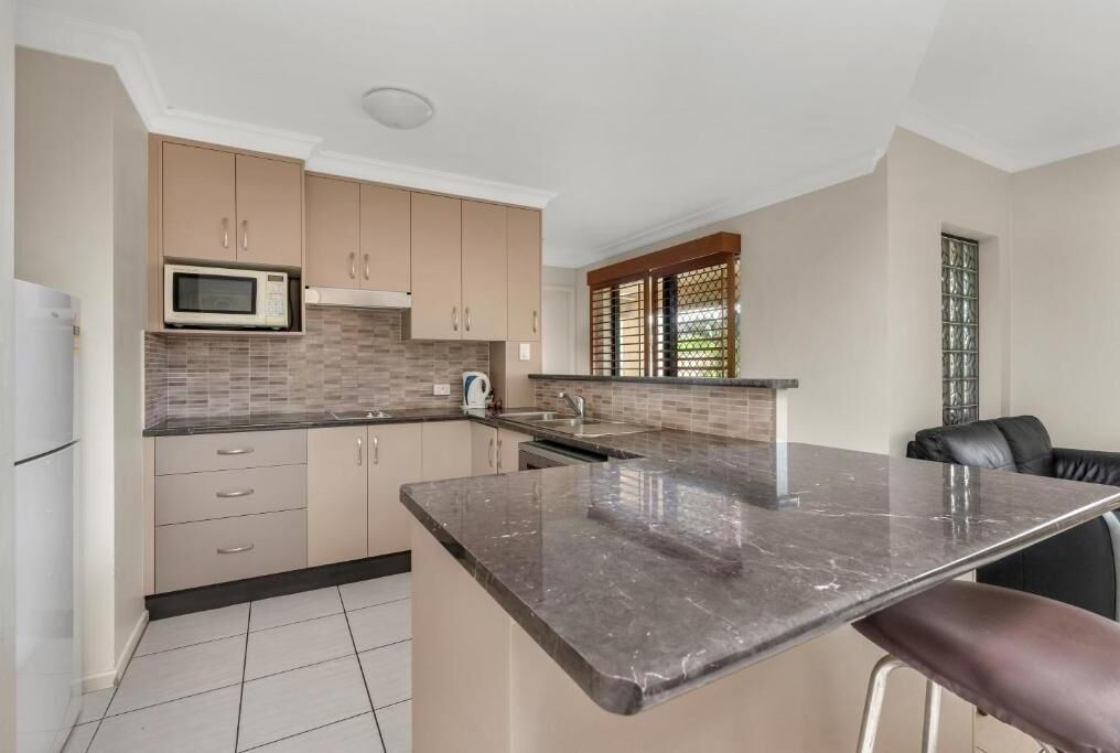 Una cocina moderna con armarios color beige, una encimera negra y un microondas.