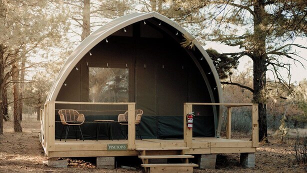 A rustic wooden tent with a covered porch, two chairs, and a small table. - Mountain Stay Under Open Skies (Torreon)