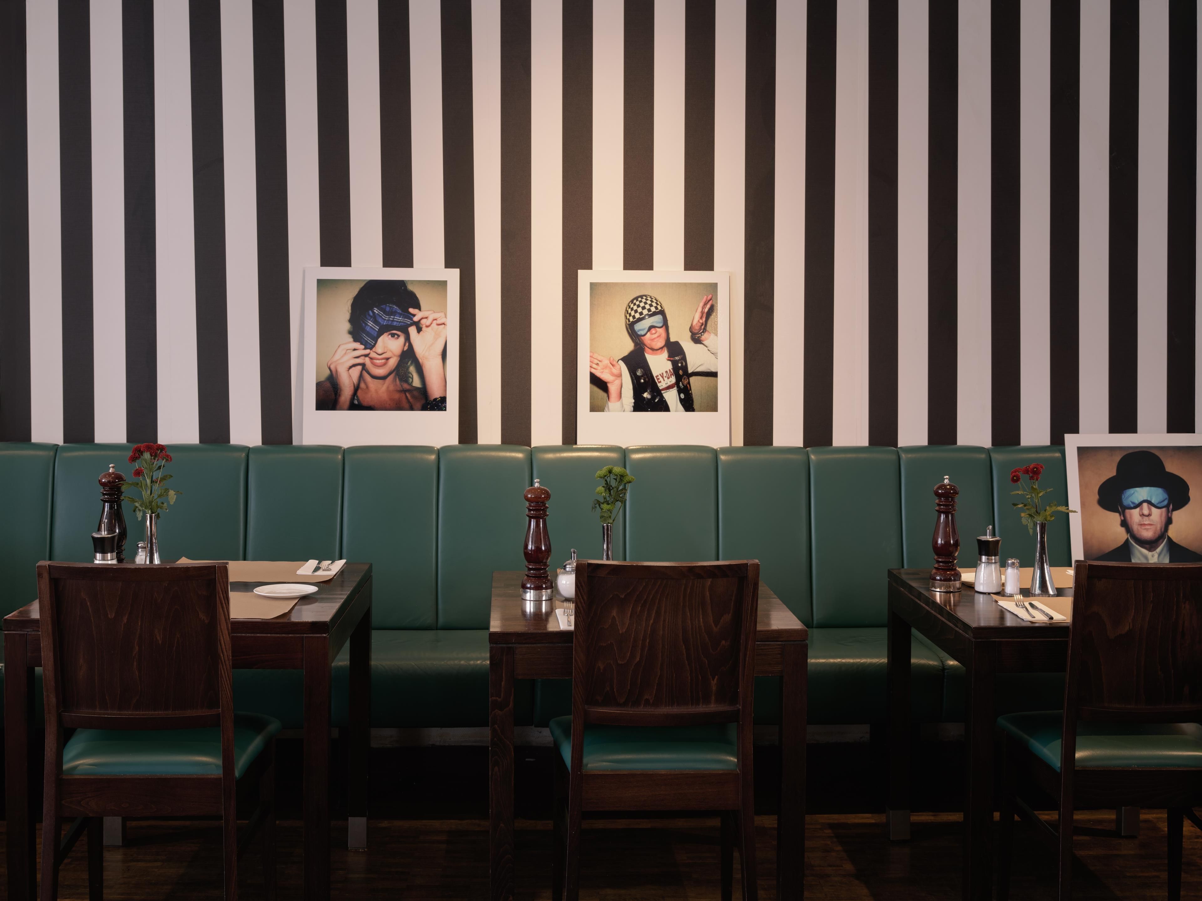 A restaurant with striped walls, green booths, wooden tables, and chairs.