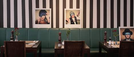 A restaurant with striped walls, green booths, wooden tables, and chairs.