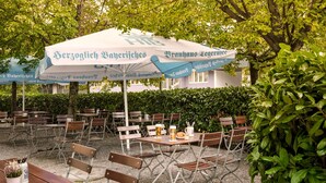 An outdoor seating area with tables and chairs, umbrellas, and a hedge in the background. - Flemings Hotel München-schwabing (Munich)