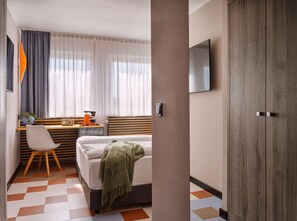 Une chambre d’hôtel comprenant un lit, un bureau avec une chaise, un téléviseur fixé au mur et une grande armoire.