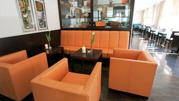 A hotel lobby with orange seating, a glass display case with bottles, and a tiled floor.