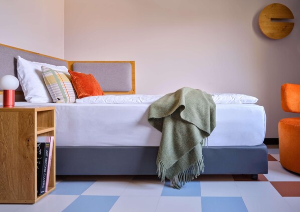 A modern bedroom with a bed, a side table, a bookshelf, and a chair. - Flemings Hotel München-schwabing (Munich)
