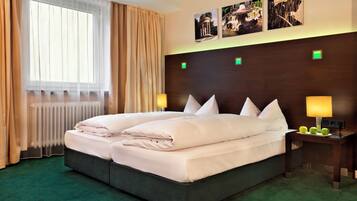 A hotel room with a large bed, two bedside lamps, a radiator, and a window with curtains.