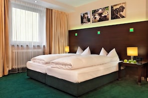 A hotel room with a large bed, two bedside lamps, a radiator, and a window with curtains. - Flemings Hotel München-schwabing (Munich)