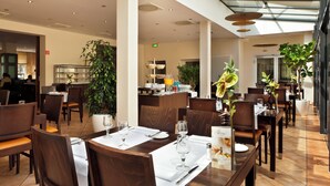 Un comedor moderno con mesas dispuestas para comensales, una zona de bar y una planta grande en maceta.