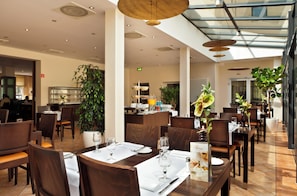 Een moderne eetruimte met gedekte tafels voor gasten, een bar en een grote potplant.