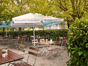 Un espace extérieur aménagé avec des tables, des chaises, des parasols et une haie en arrière-plan.