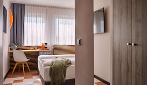 Una habitación de hotel con una cama, un escritorio con una silla, una cafetera y un televisor en la pared.