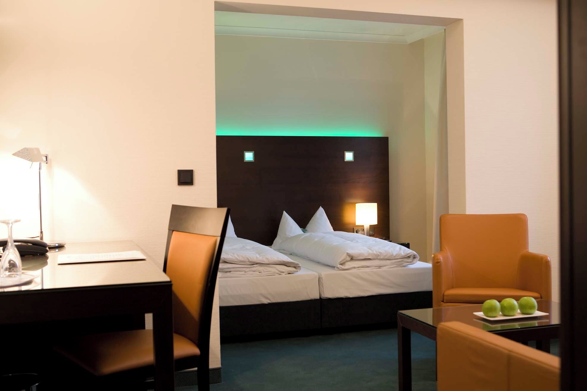 A hotel room with a bed, a desk, a chair, and a small table with apples.