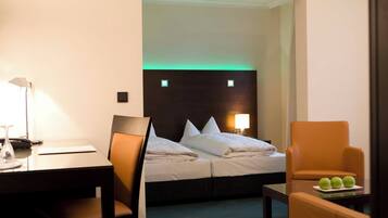 A hotel room with a bed, a desk, a chair, and a small table with apples.