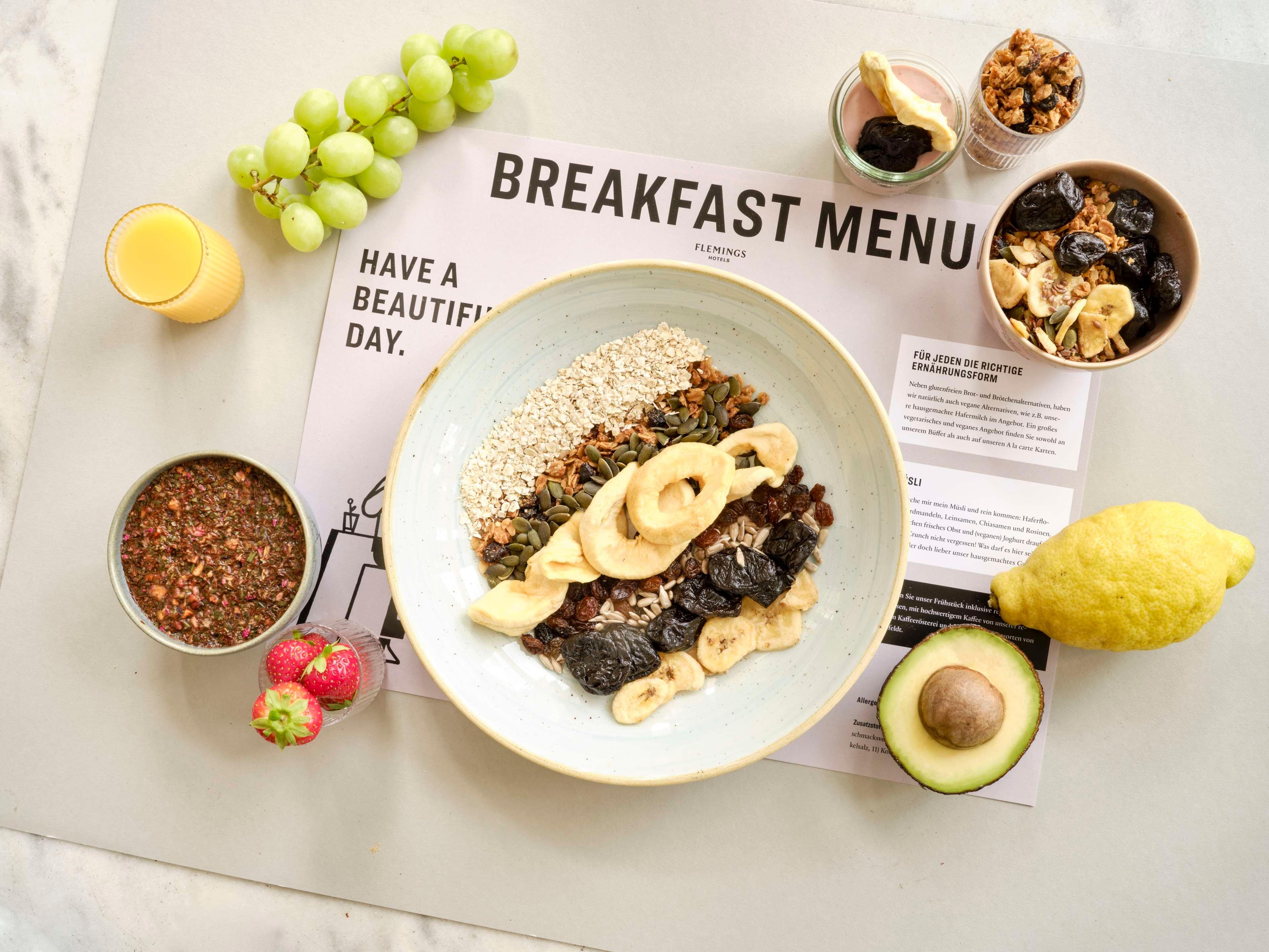 A breakfast plate with various toppings, a glass of orange juice, a bowl of granola, a jar of jam, and a half-cut avocado on a table with a breakfast menu.