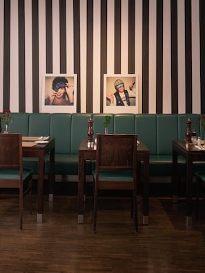 Interior de restaurante con asientos tapizados en verde, mesas de madera y decoración de pared a rayas.