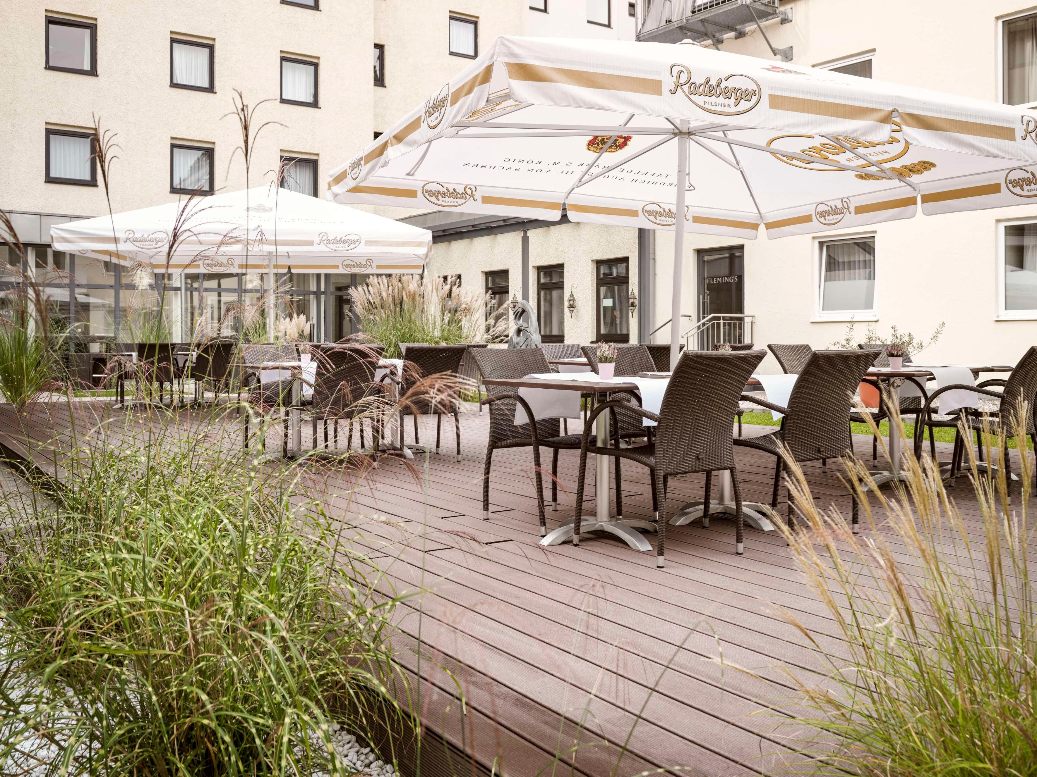 An outdoor seating area with tables and chairs, umbrellas, and a building in the background.