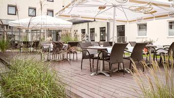 An outdoor seating area with tables and chairs, umbrellas, and a building in the background.