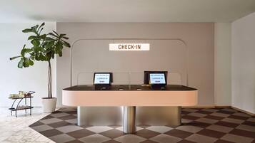 A check-in counter with two computer stations, a potted plant, and a small table with jars and rolled towels.