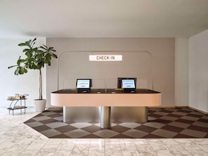 A check-in counter with two computer stations, a potted plant, and a small table with jars and rolled towels. - Flemings Hotel München-schwabing (Munich)