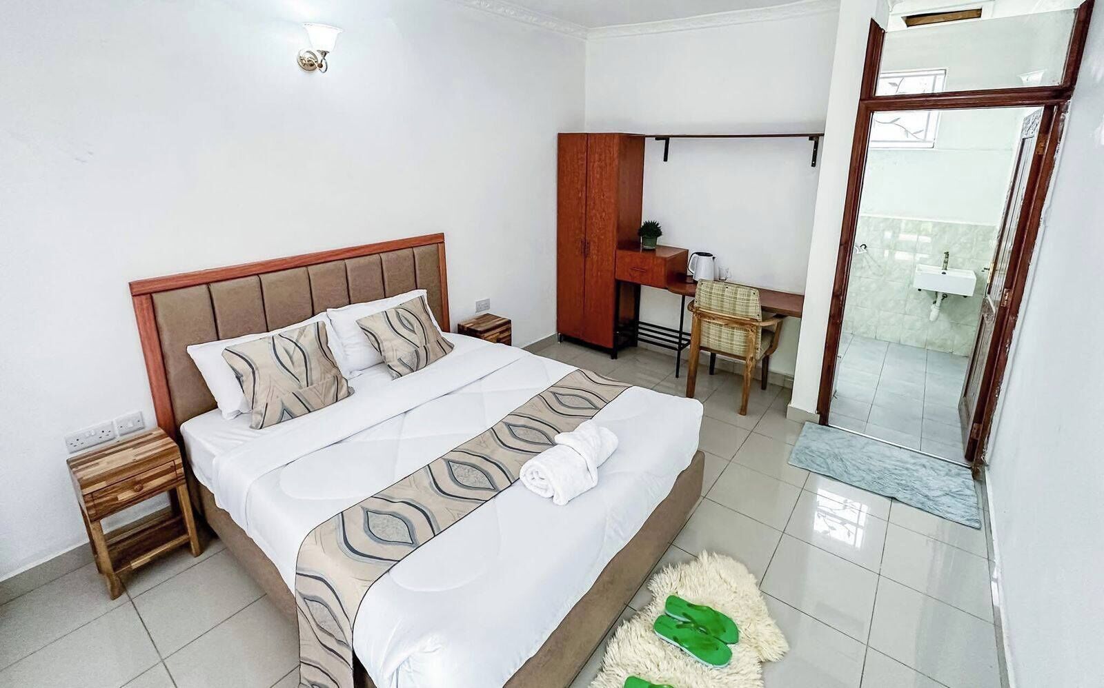 A hotel room with a bed, a desk, a chair, a small table, and a mirror.
