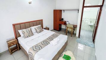 A hotel room with a bed, a desk, a chair, a small table, and a mirror.