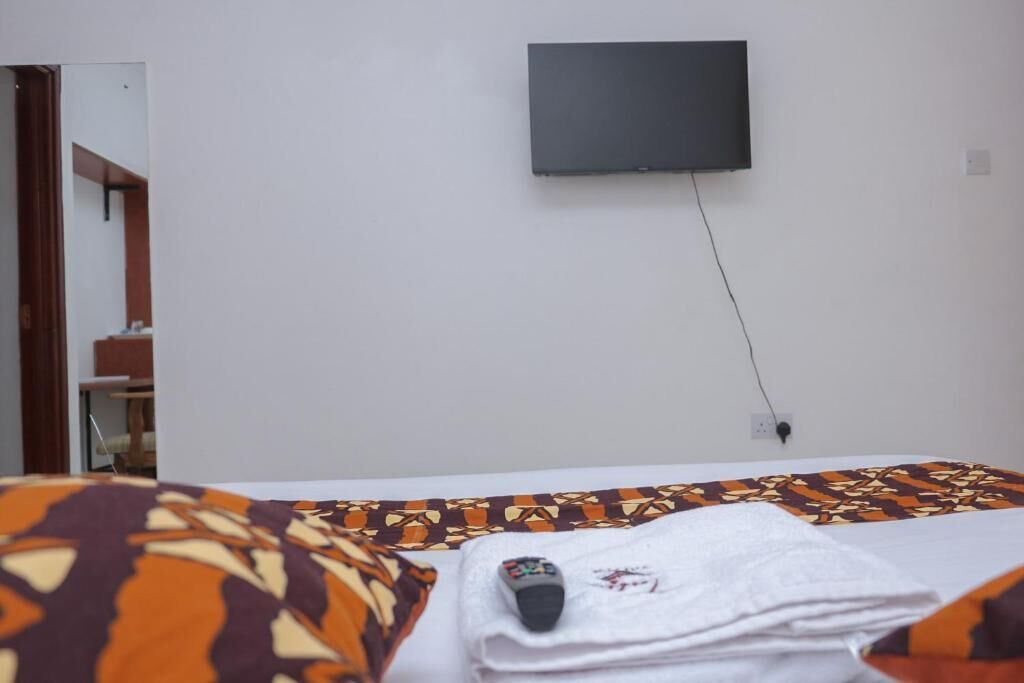 Habitación de hotel con una cama, un televisor montado en la pared y una puerta que da a otra habitación.